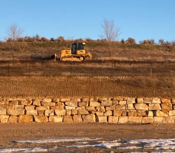 retaining wall holding back dirt with yellow CAT excavator in background