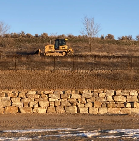 retaining wall holding back dirt with yellow CAT excavator in background